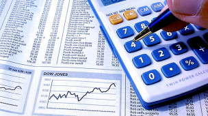 Como encontrar o ponto de equilíbrio financeiro da sua empresa. A imagem mostra uma mão usando a calculadora sobre uma folha de jornal com índices de bolsa de valores.