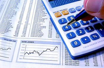 Como encontrar o ponto de equilíbrio financeiro da sua empresa. A imagem mostra uma mão usando a calculadora sobre uma folha de jornal com índices de bolsa de valores.